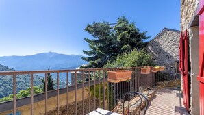 A balcony with a view of mountains, a stone building with red shutters, and a metal railing. - Gîte Madres Coronat Balcon du Canigou (Jujols)