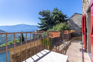 A balcony with a view of mountains, a stone building with red shutters, and a metal railing. - Gîte Madres Coronat Balcon du Canigou (Jujols)