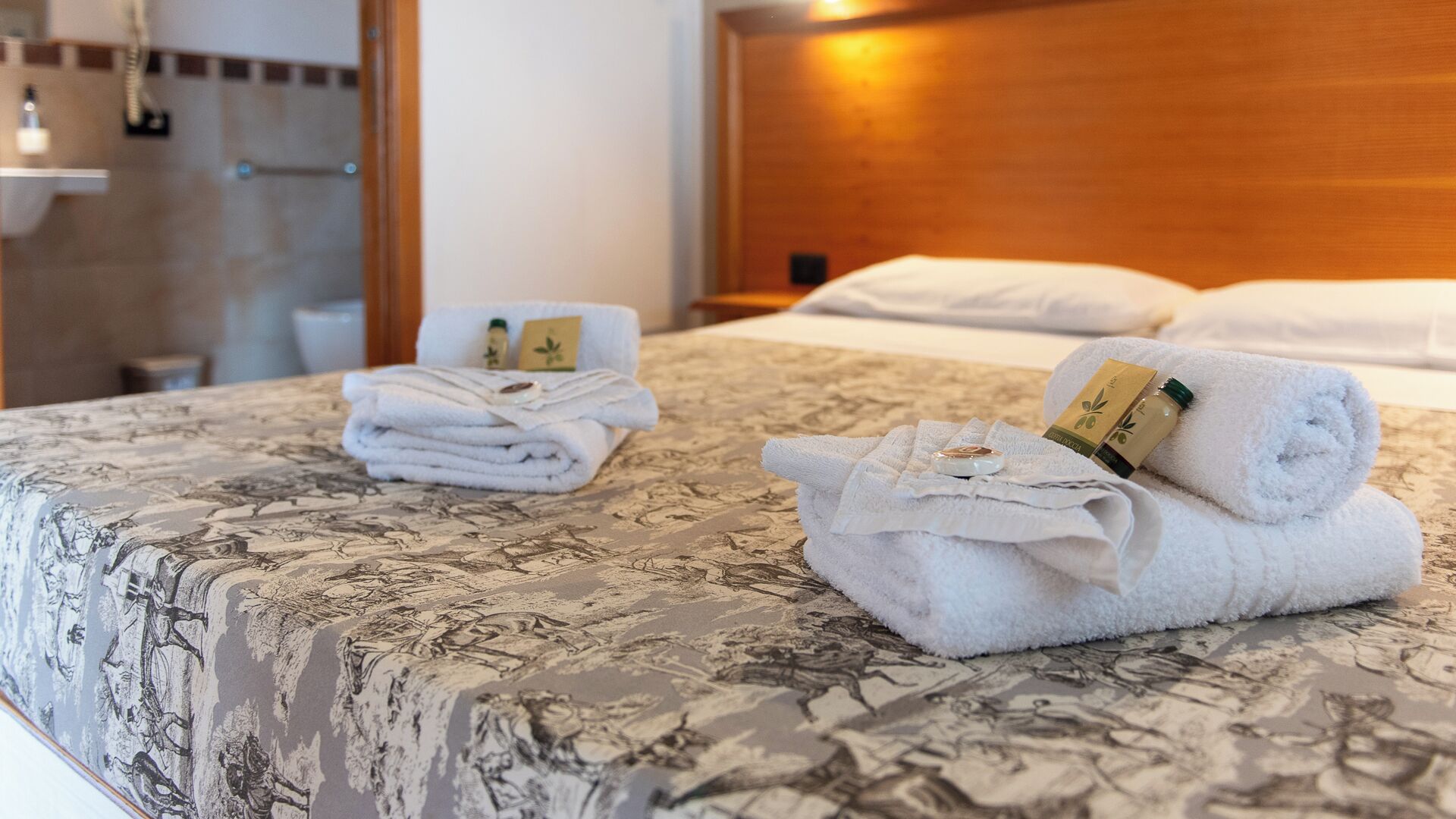 A hotel room with a bed, neatly folded towels, and a bathroom visible in the background.