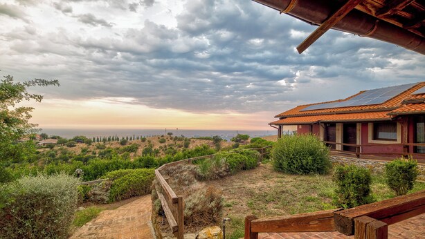 A house with a sloped roof and solar panels, surrounded by a stone wall and lush greenery. - Tenuta dell'Argento by Rentbeat (Civitavecchia)