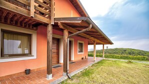 A house with a wooden balcony, a brick pathway, and a view of green hills. - Tenuta dell'Argento by Rentbeat (Civitavecchia)