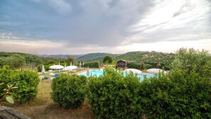 A pool area with umbrellas and lounge chairs, surrounded by lush greenery and hills in the background. - Tenuta dell'Argento by Rentbeat (Civitavecchia)
