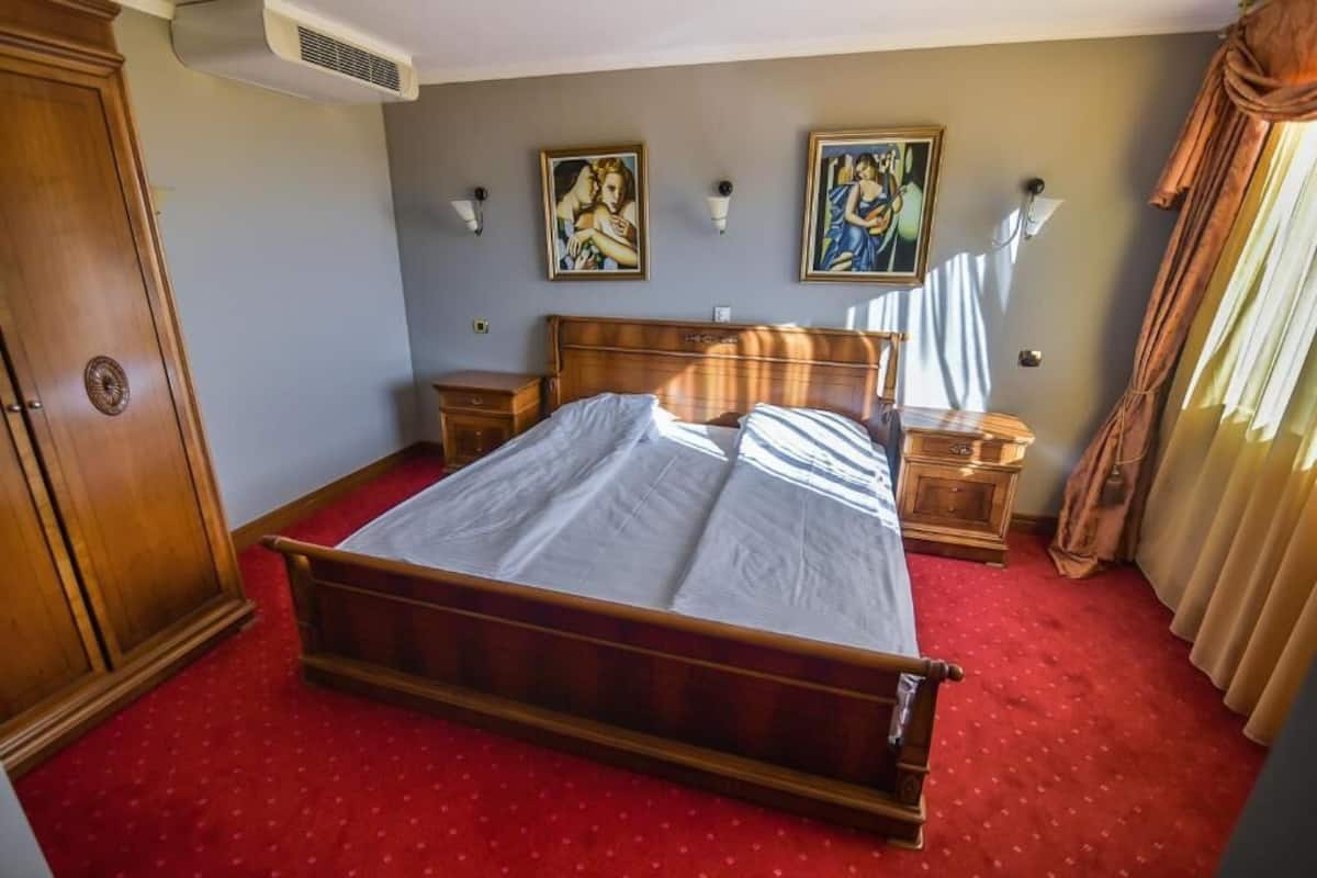 Een hotelkamer met een houten bed, twee nachtkastjes, een kledingkast en twee wandlampen.