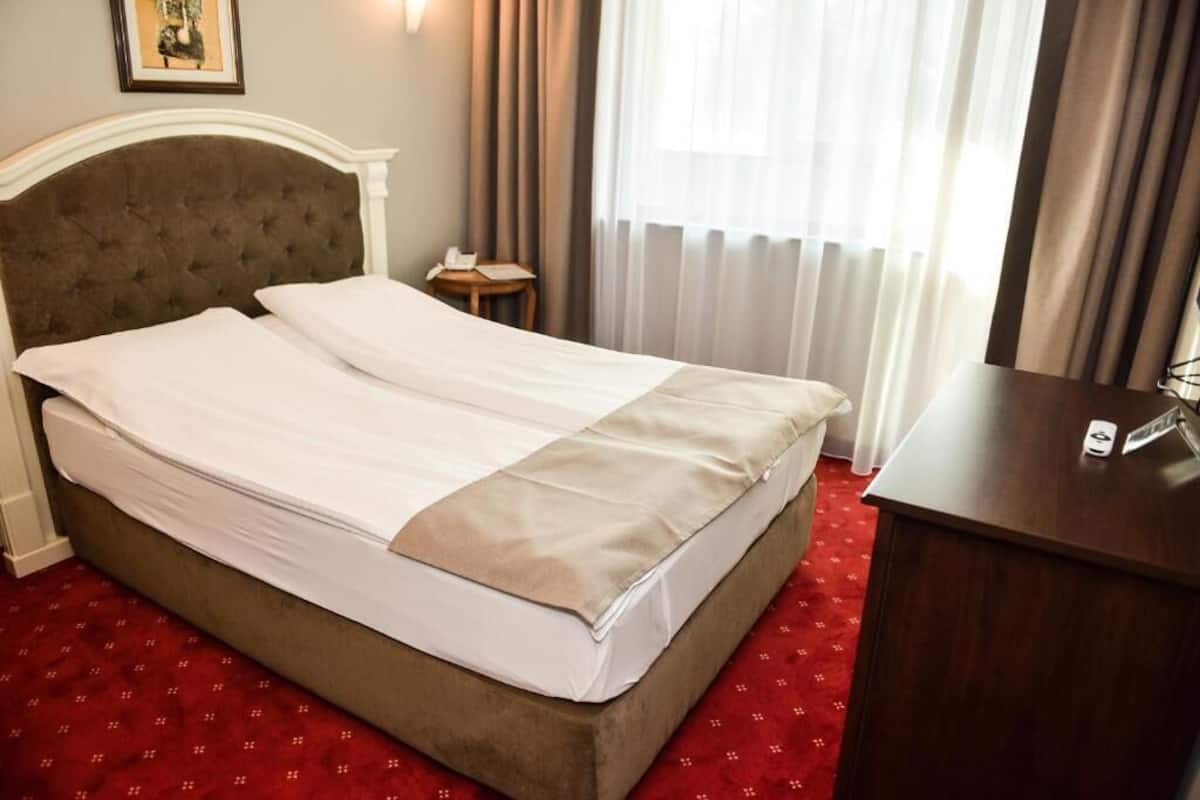Een hotelkamer met een tweepersoonsbed, een houten nachtkastje, een bureau en een raam met gordijnen.