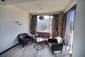 A modern living room with a sofa, two armchairs, a glass coffee table, and a chandelier. - Hotel Skalite (Belogradchik)