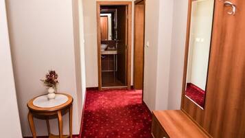Un estrecho pasillo con alfombra roja, un banco de madera, una mesita redonda con un florero y un espejo en la pared.
