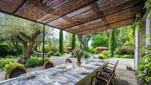 An outdoor dining area with a long table set for six, surrounded by wicker chairs, under a shaded pergola. - Villa N1 Saint-Émilion (Saint-Émilion)
