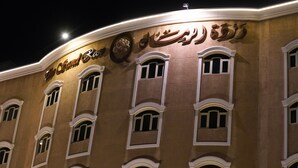 A building with a curved facade, multiple windows with white frames, and illuminated signage. - Sand Rose Suite Hotel (Al Khobar)