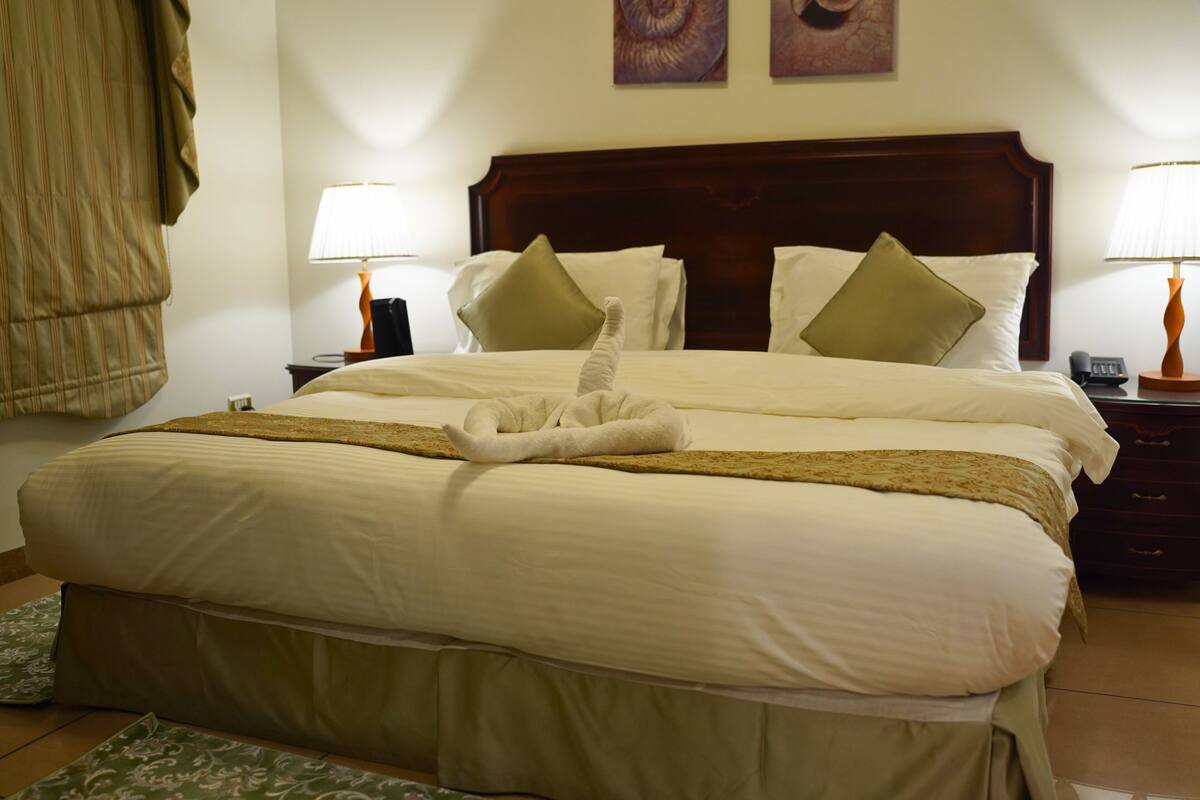 Ein ordentlich bezogenes Bett mit Handtuch, zwei Kissen und einem Holzkopfteil in einem Hotelzimmer.
