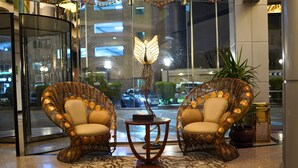 A lobby with two wicker chairs, a table, and a decorative light fixture. - Sand Rose Suite Hotel (Al Khobar)