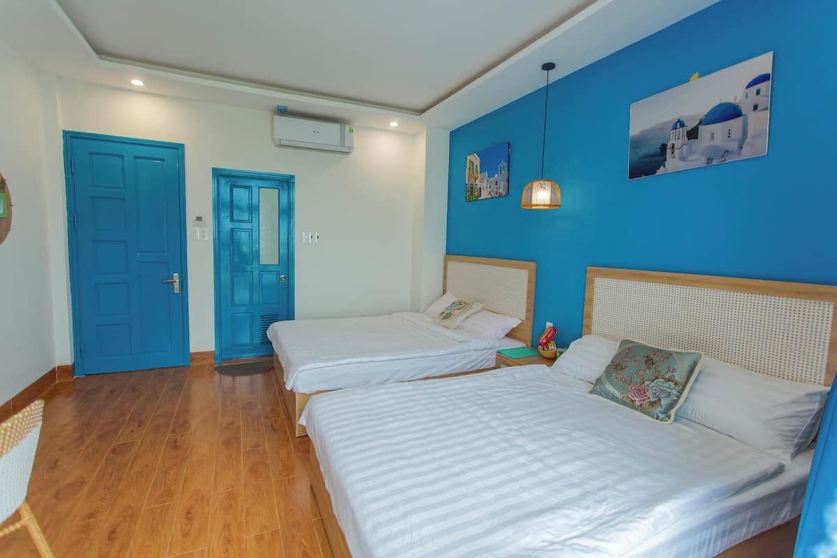 Habitación de hotel con dos camas, una pared azul y un cuadro de una escena costera.