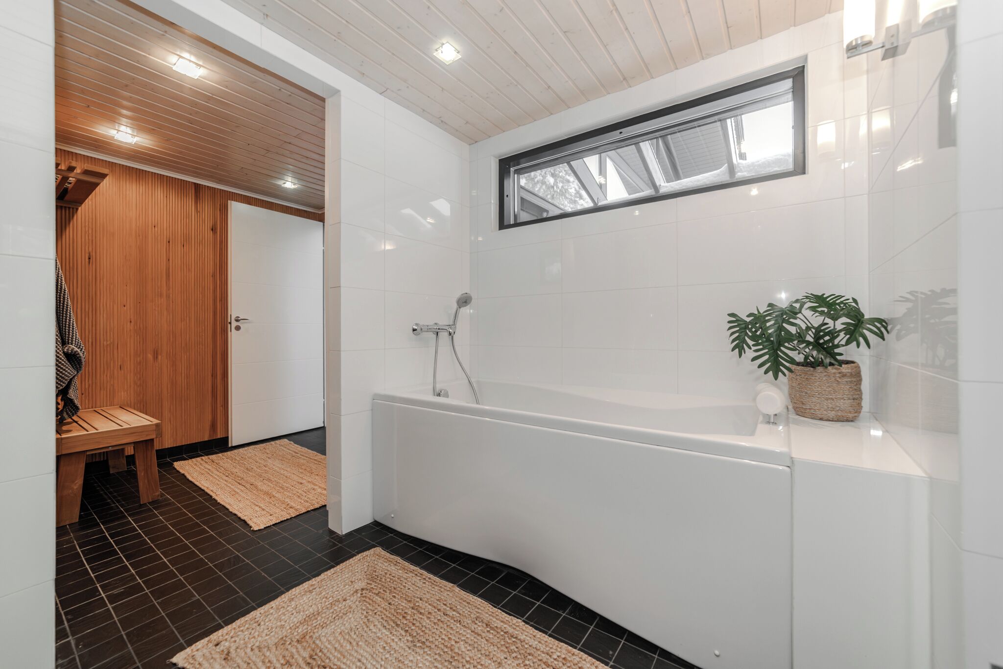 Une salle de bain moderne avec une baignoire, un banc en bois et une plante en pot.
