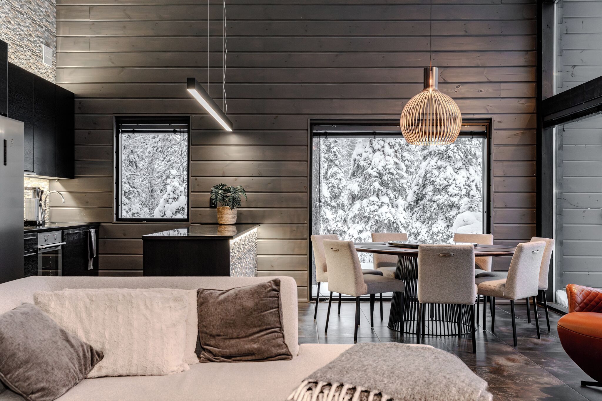 Un intérieur moderne avec un plafond en bois, un coin repas comprenant des chaises et une table, et un canapé agrémenté de coussins.