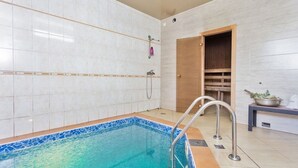 A swimming pool with a tiled deck, a shower area, and a wooden bench with a bowl of leaves.