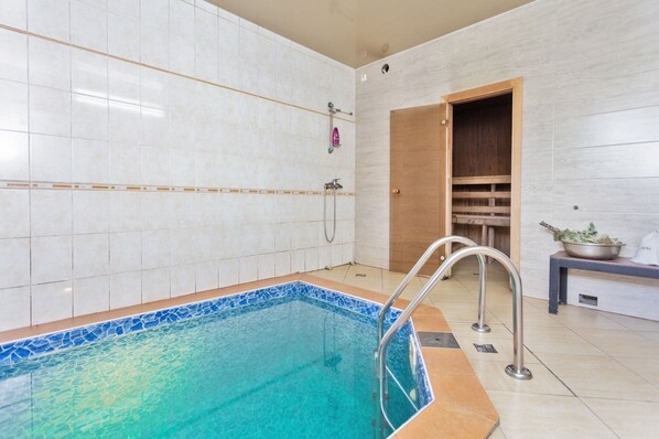 A swimming pool with a tiled deck, a shower area, and a wooden bench with a bowl of leaves.