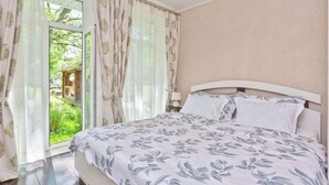 A bedroom with a bed, curtains, and a view of greenery outside.