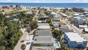 Uma área residencial costeira com várias casas de dois andares, uma piscina visível e uma praia ao fundo.