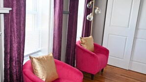 A room with two pink armchairs, one with a gold pillow, and a modern floor lamp.