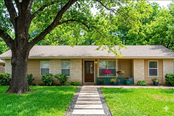 A single-story house with a stone facade, a front door, and a small porch with potted plants. - Spacious 3BR SoCO Family Home❤️ Big Private Yard with Firepit | Minutes to DT (Austin)