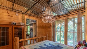 A wooden cabin room with a large bed, a chandelier, and a view of the outdoors. - Mamas Mountain Place -custom home, pet friendly, hot tub, large entertain room with foosball, pond (Seven Devils)