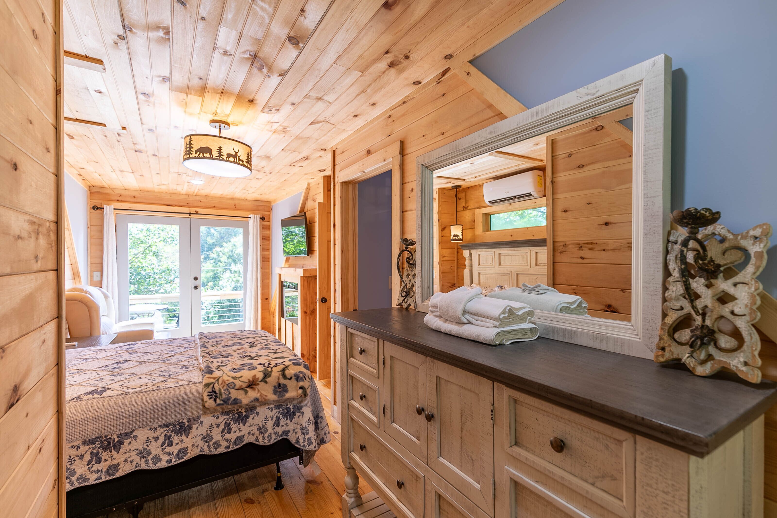 Habitación de una cabaña de madera con cama, cómoda y espejo grande.