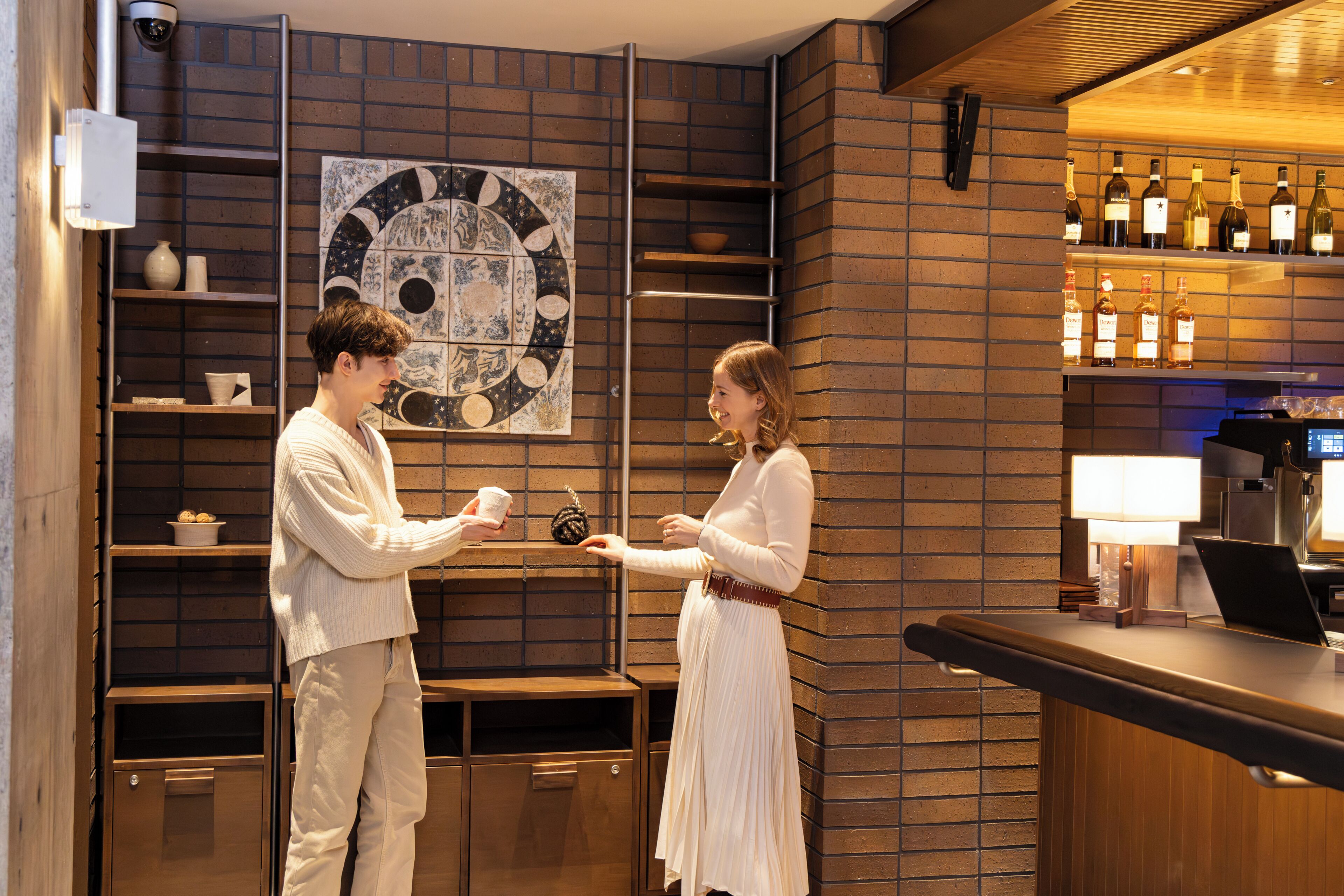 A bar area with a brick wall, a large circular artwork, and shelves with bottles.