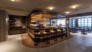 Un área de bar moderna con una barra curva, taburetes y una zona de estar con mesas y sillas.