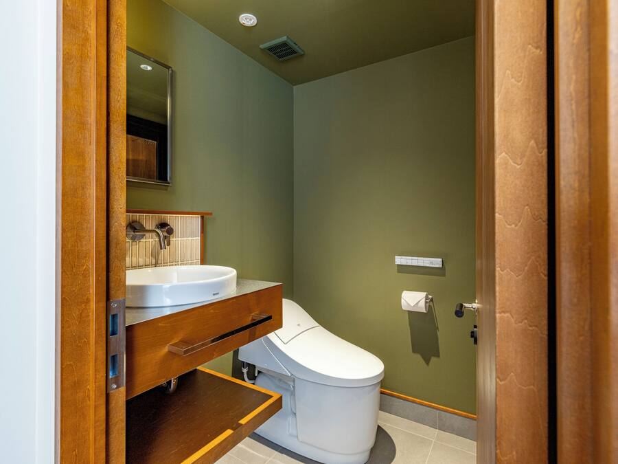 A bathroom with a white toilet, a wooden vanity, a mirror, and a wall-mounted toilet paper holder.