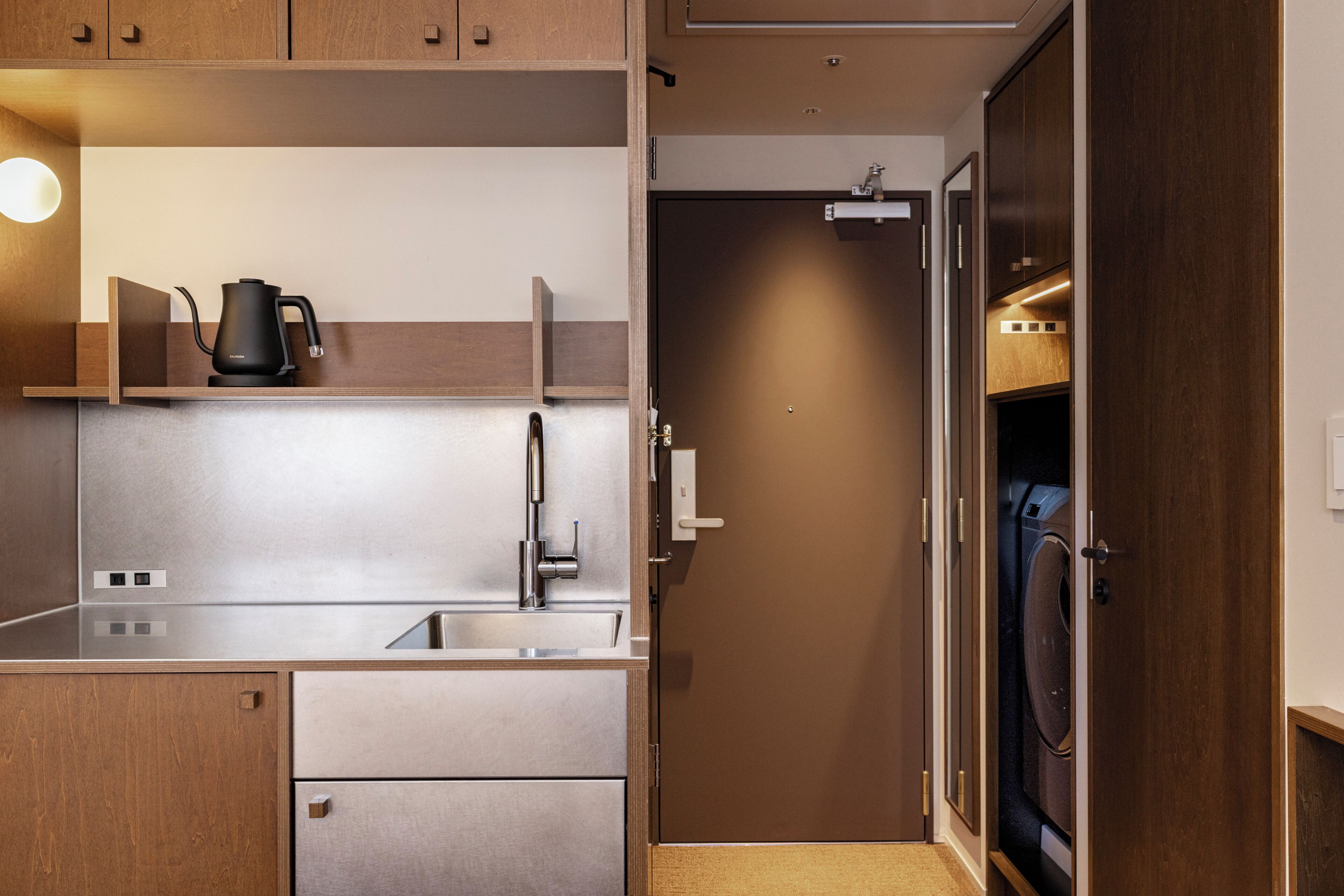 A compact kitchen with a modern faucet, a kettle, and a built-in washing machine.