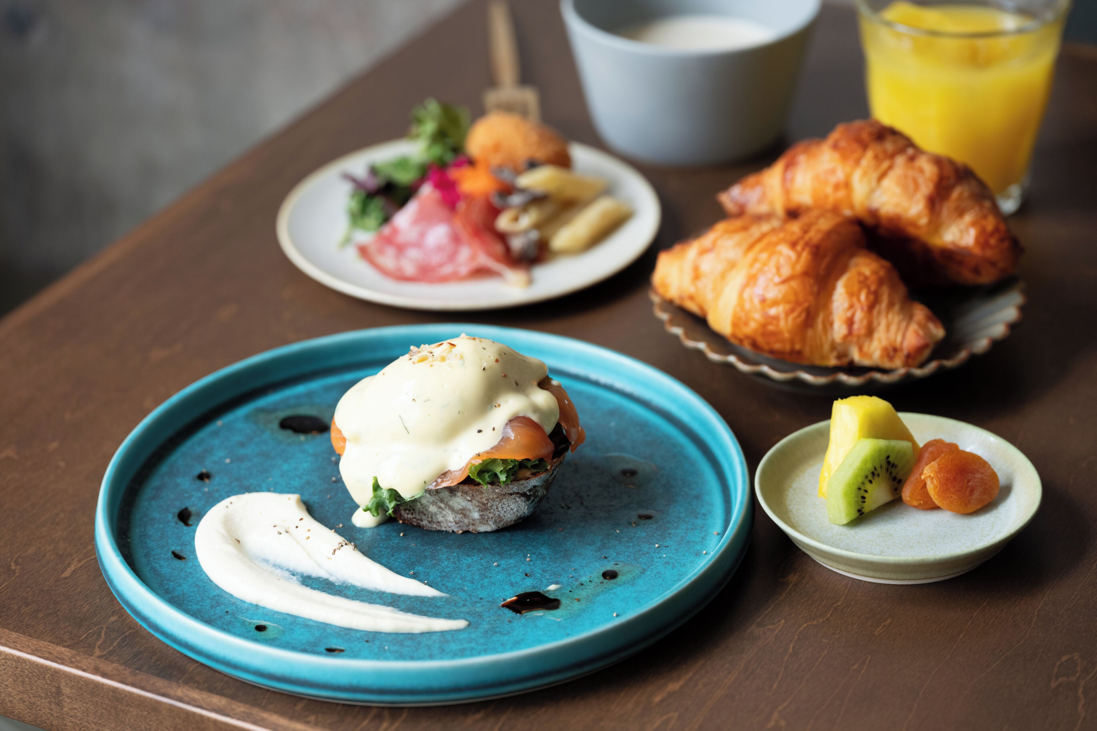 A table with a plate of food, a croissant, and a glass of orange juice.
