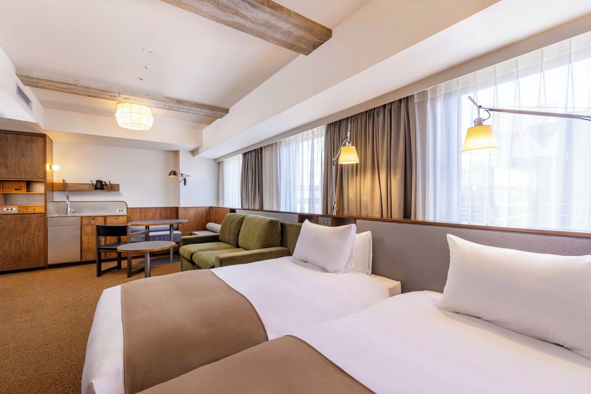 A hotel room with a bed, a desk, a chair, a sofa, and a window with curtains.