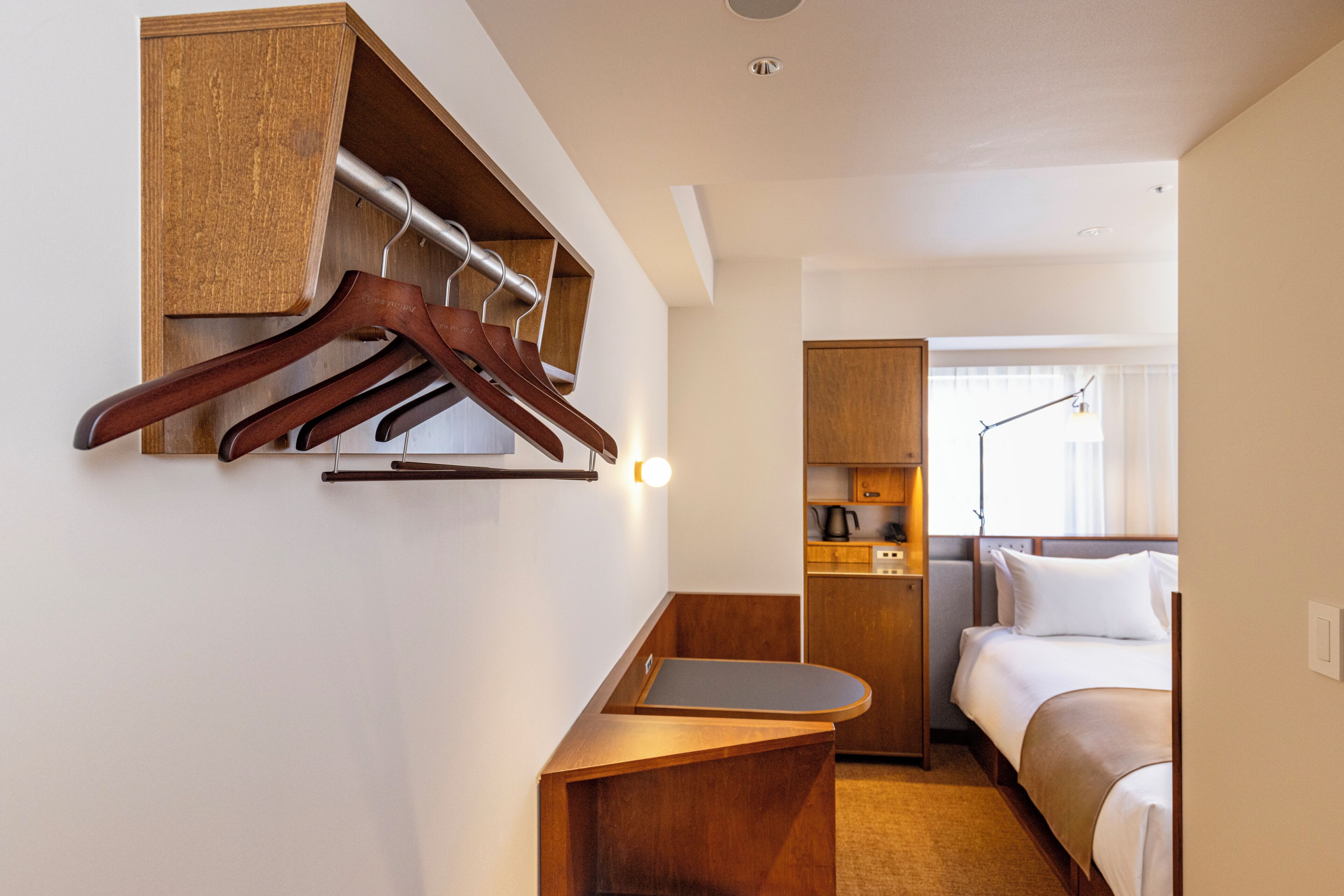 Ett hotellrum med en säng, ett skrivbord, en spegel, en klädställning och ett litet kök.