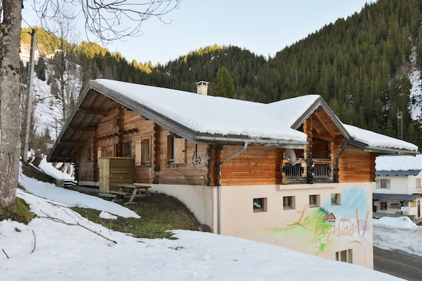Un chalet en bois dotĂ© dâun balcon, entourĂ© de neige et de montagnes boisĂ©es.