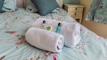 Una cama bien hecha con ropa de cama floral, una almohada azul y una mesita de noche pequeña con una lámpara.
