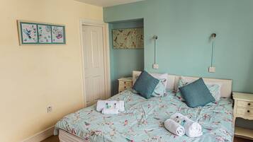 A bedroom with a floral bedspread, two pillows, a nightstand, and a wall art piece.