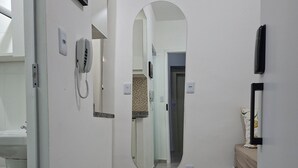 Un couloir avec un mur blanc, un miroir rond, un téléphone et une porte donnant sur une autre pièce.