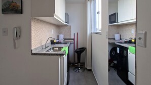 Une cuisine compacte avec des meubles blancs, un plan de travail en granit, un évier et une petite chaise noire.