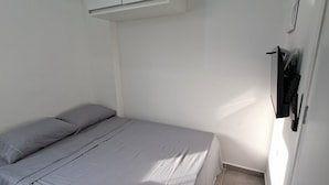Une petite chambre avec un lit simple, une couvre-lit grise, un plafond blanc et une armoire blanche.