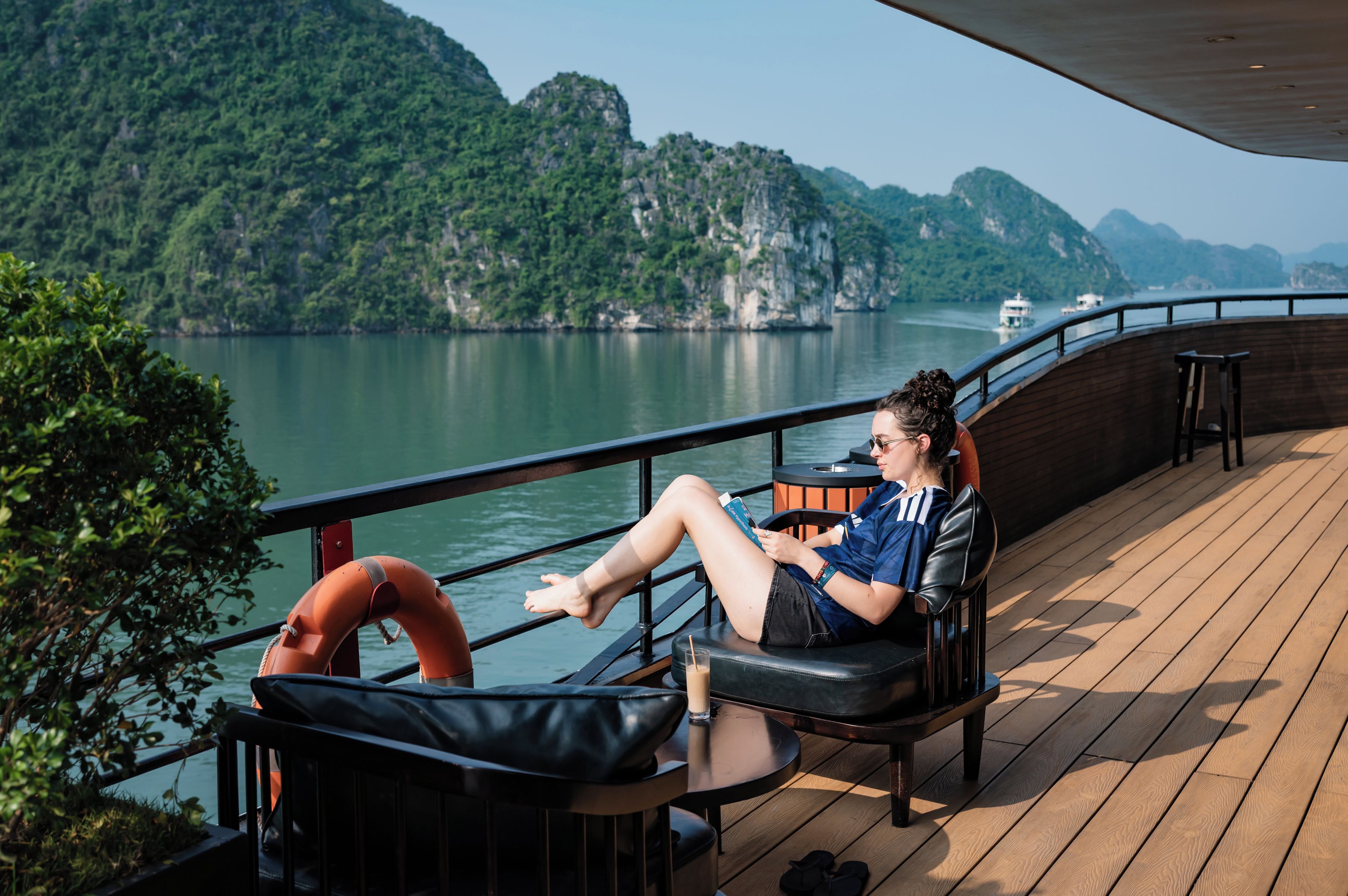 A person seated on a deck chair with a view of a body of water and mountains in the background.