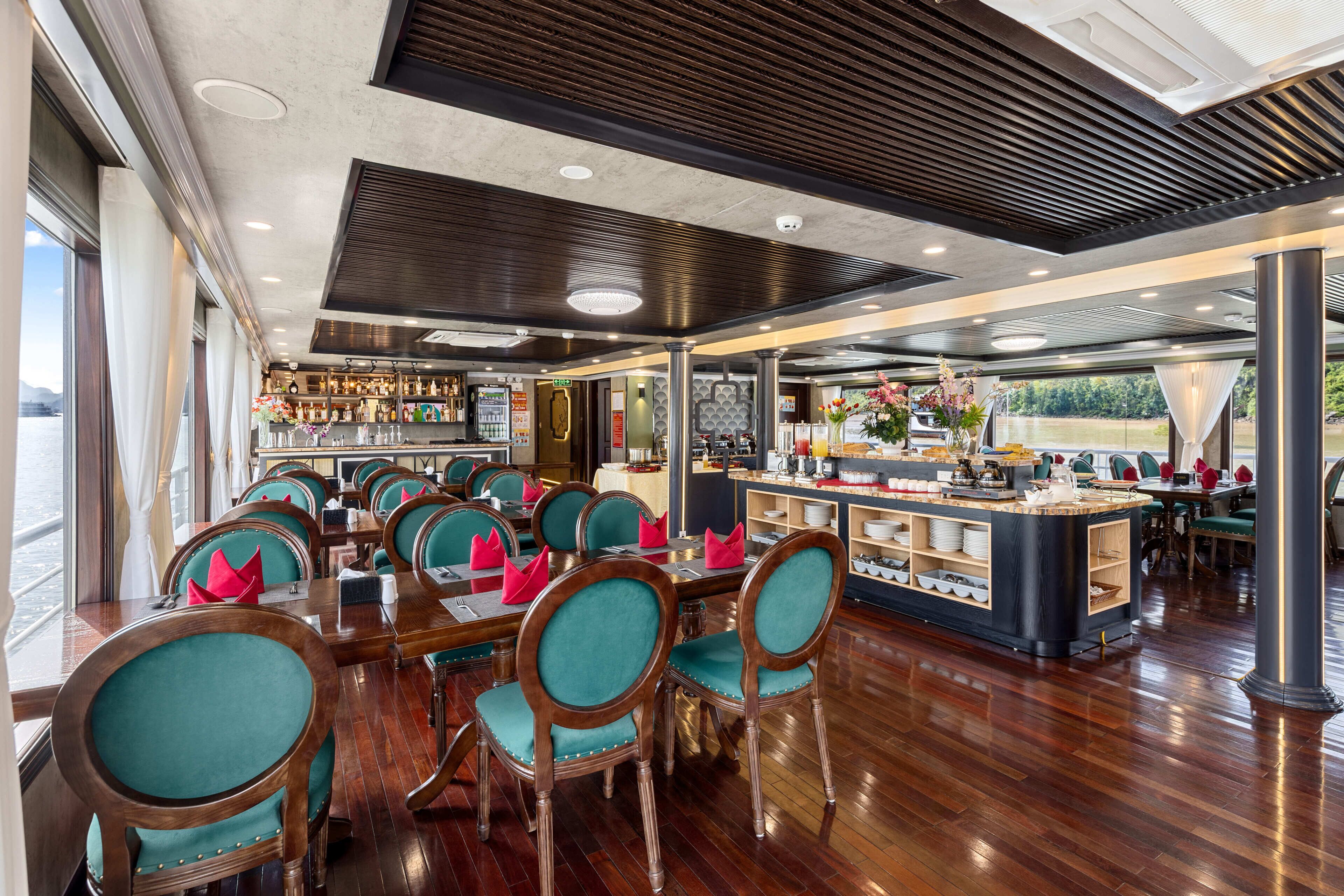 Un restaurante con piso de madera, sillas tapizadas en color verde azulado y una zona de bar con vista al exterior.