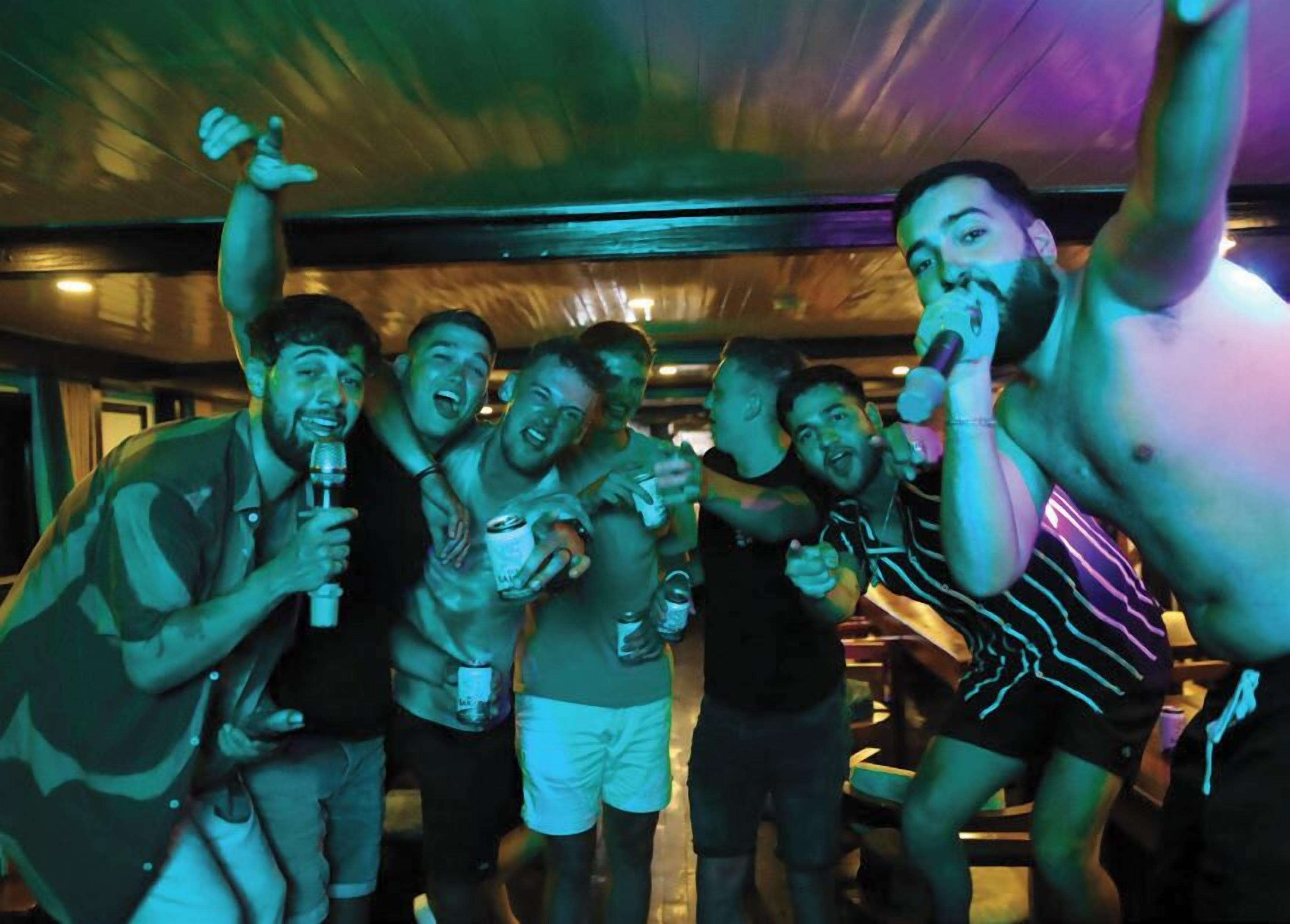 A group of people in a dimly lit room with a wooden ceiling, some holding drinks.