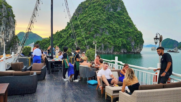 A deck with outdoor seating, a railing, and a view of a green island and water. - Oasis Bay Party Cruise (Tuan Chau)
