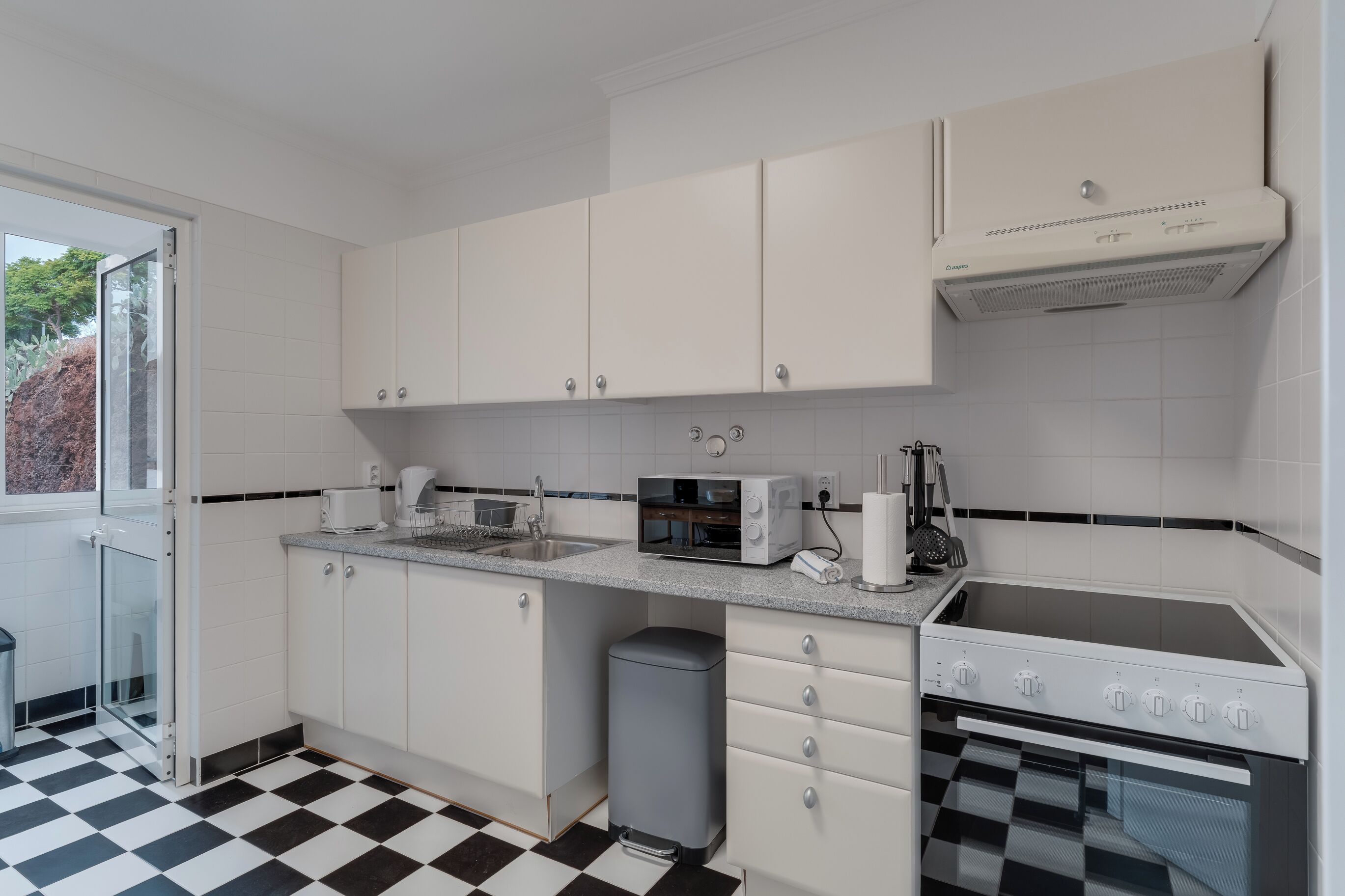 Une cuisine moderne avec des meubles blancs, un four à micro-ondes, une cuisinière et une poubelle.