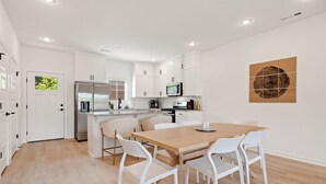 Una cocina moderna con muebles blancos, una mesa de comedor de madera y sillas blancas.