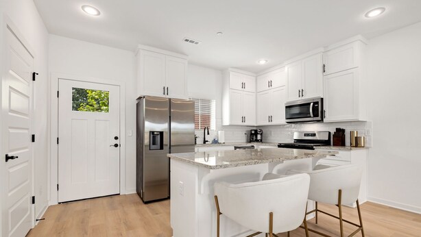 Una cocina moderna con armarios blancos, electrodomésticos de acero inoxidable y una isla central con taburetes de bar.