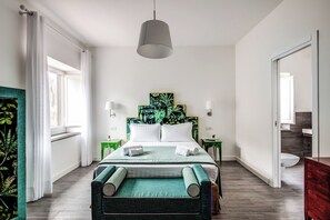Une chambre d’hôtel moderne avec un grand lit, un banc recouvert d’un tissu vert, un luminaire au plafond et une vue sur la salle de bain.