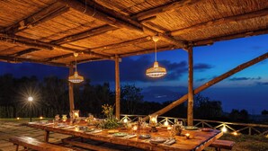 An outdoor dining area with a long wooden table set for a meal, under a wooden pergola with hanging lights. - Villa Aprea - luxury villa with stunning views and private heated pool (Massa Lubrense)