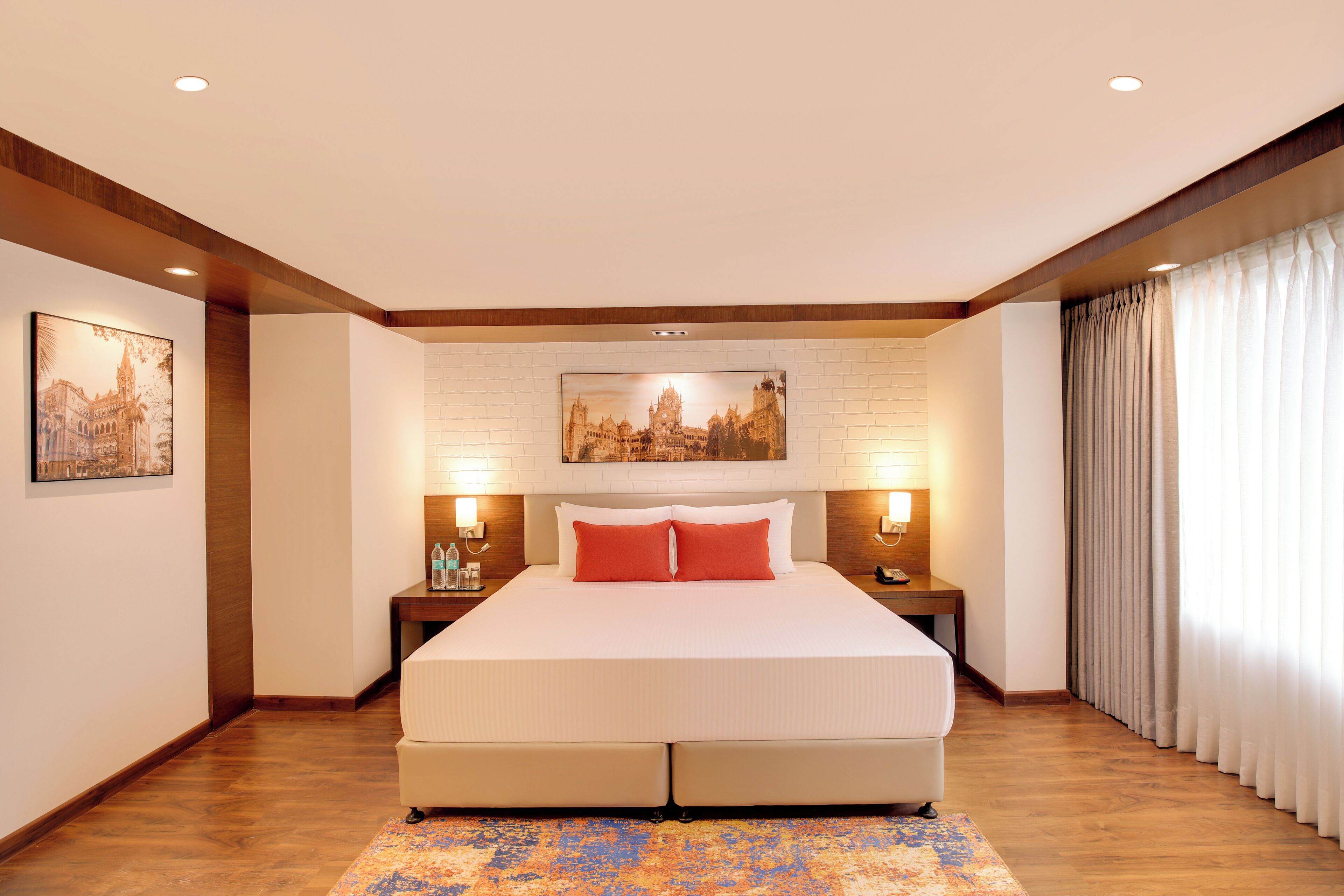 Un'ampia camera d'albergo con un letto grande, pavimento in legno e un quadro con una veduta cittadina sopra il letto.