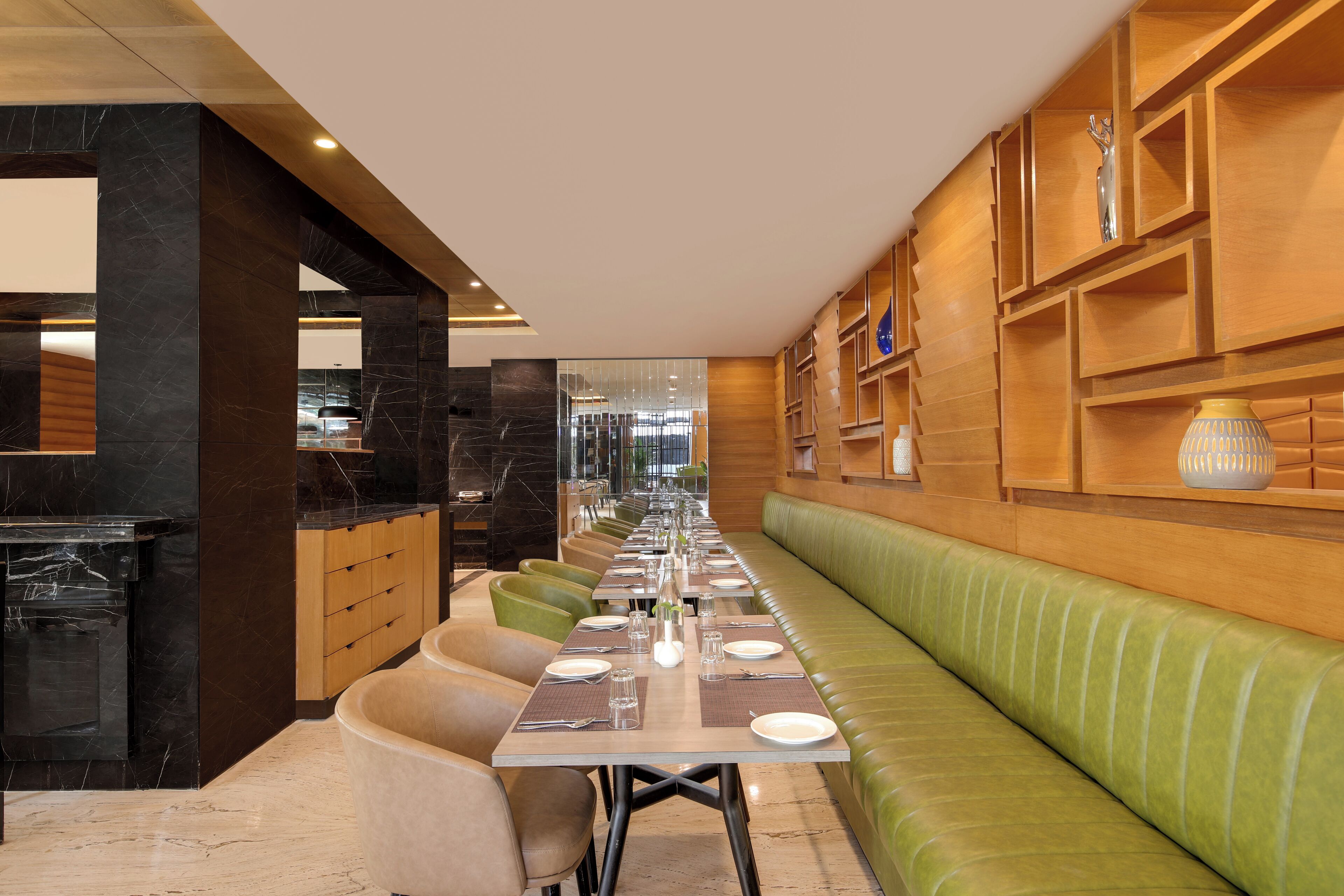 Un ristorante moderno con un lungo tavolo da pranzo, sedute imbottite verdi ed elementi decorativi su mensole in legno.