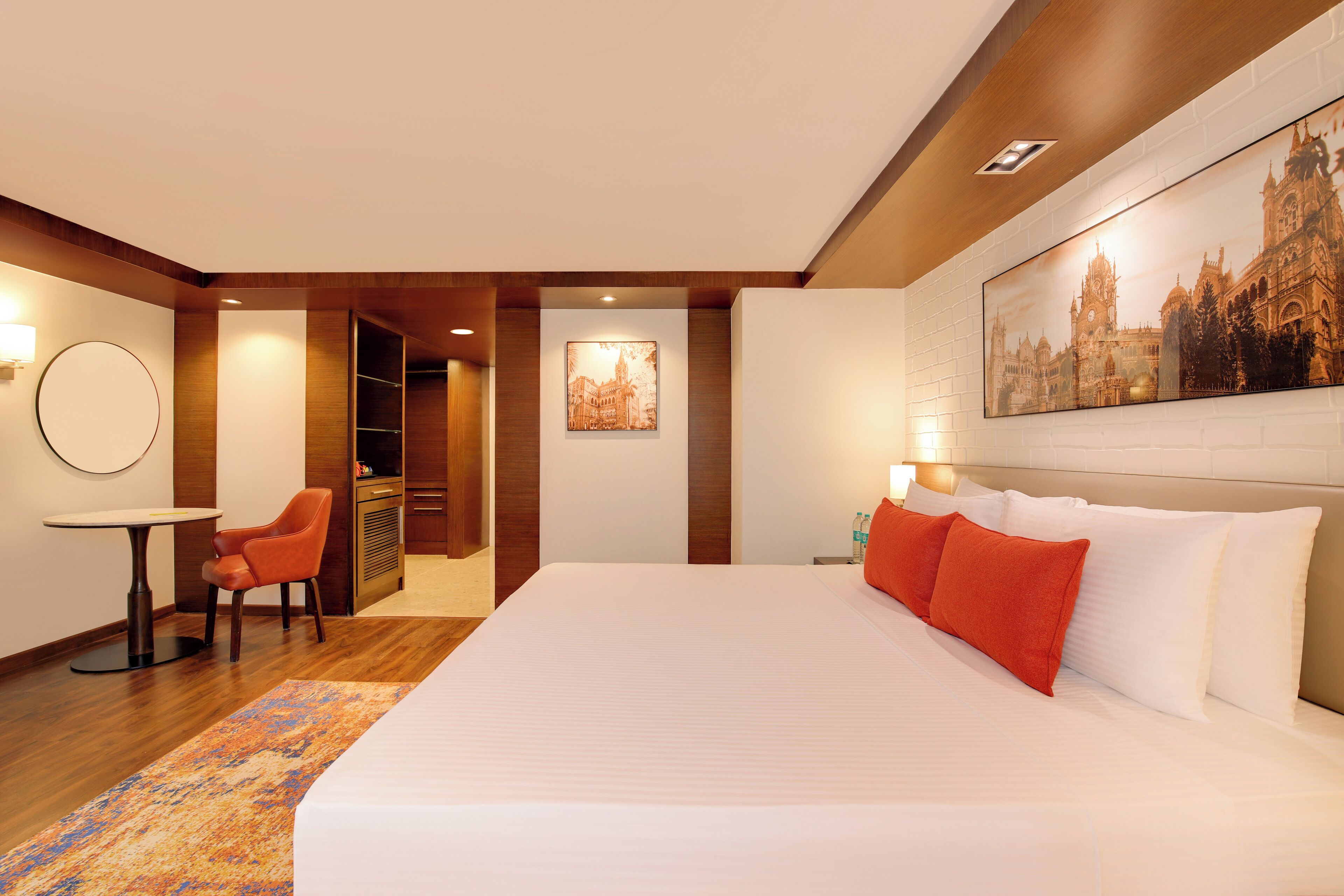 A hotel room with a large bed, a desk, a chair, and a painting on the wall.